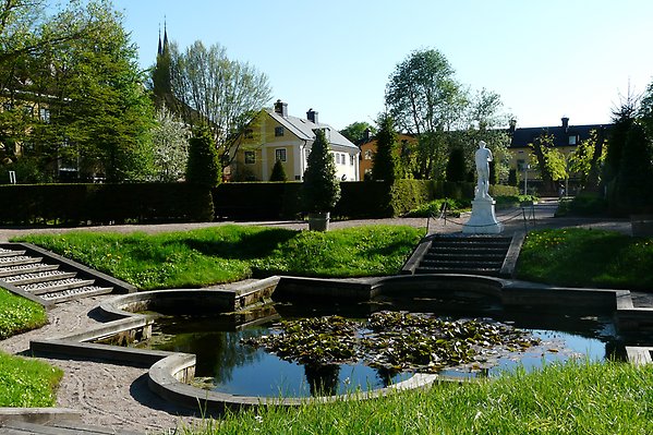 Pond surrounded by greenery. In the background is a white statue and a building.