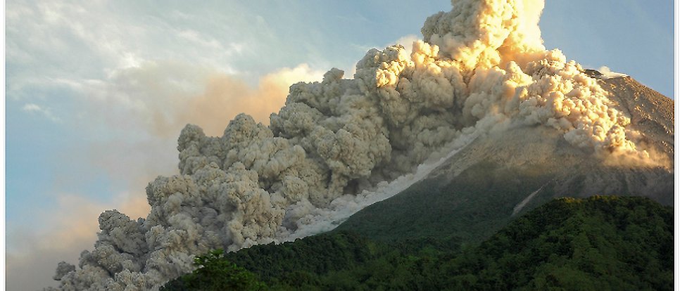 Volcano with a large cloud of smoke rolling down from its top.