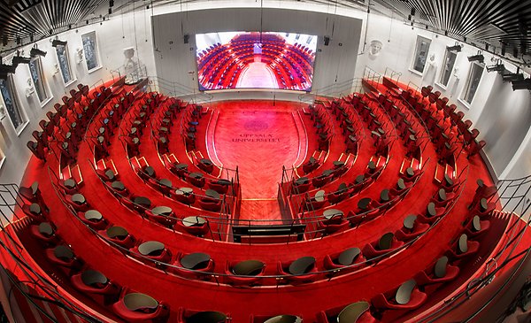 Rows of chairs form a semicircle around a stage and a large screen. On the stage floor it says Uppsala University.