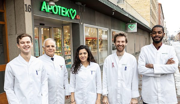 A group of pharmacy alumni in white lab coats outside of a pharmacy