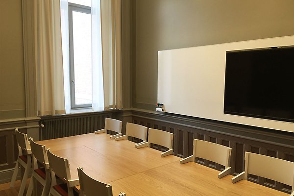 A seminar room with a table and a screen and white board.